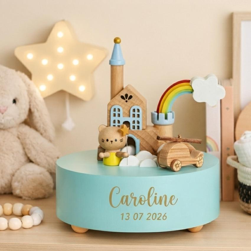 Boîte à musique en bois personnalisée Caroline avec décor maison, chat, arc-en-ciel et date de naissance dans une chambre bébé chaleureuse